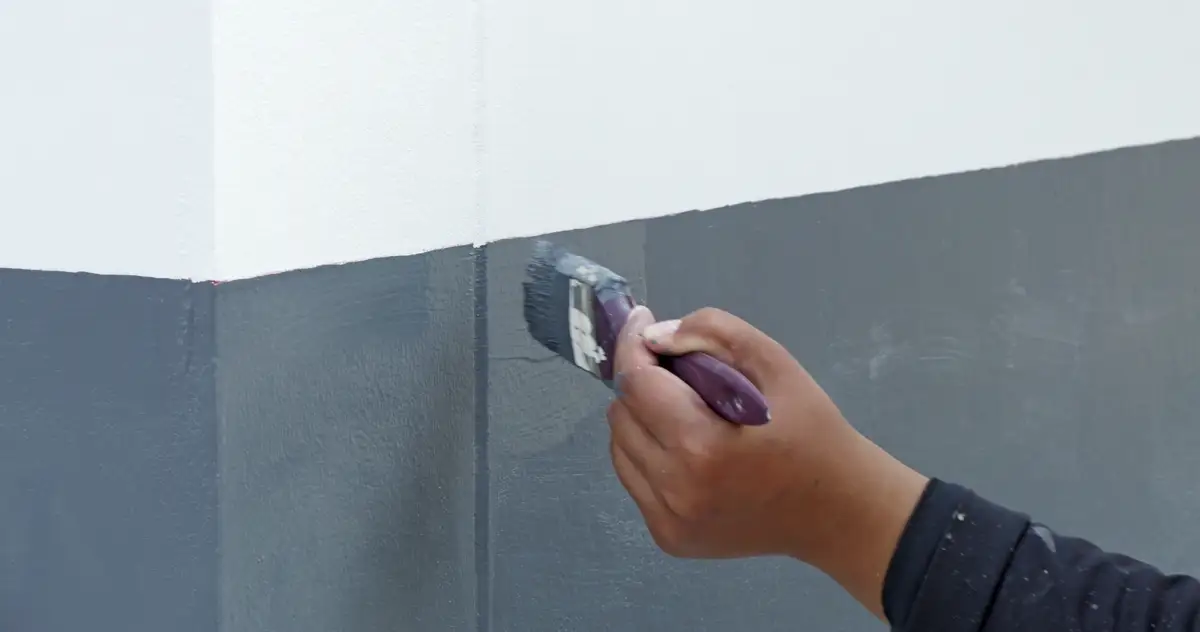 Painter cutting a line between a navy lower wall and white upper wall