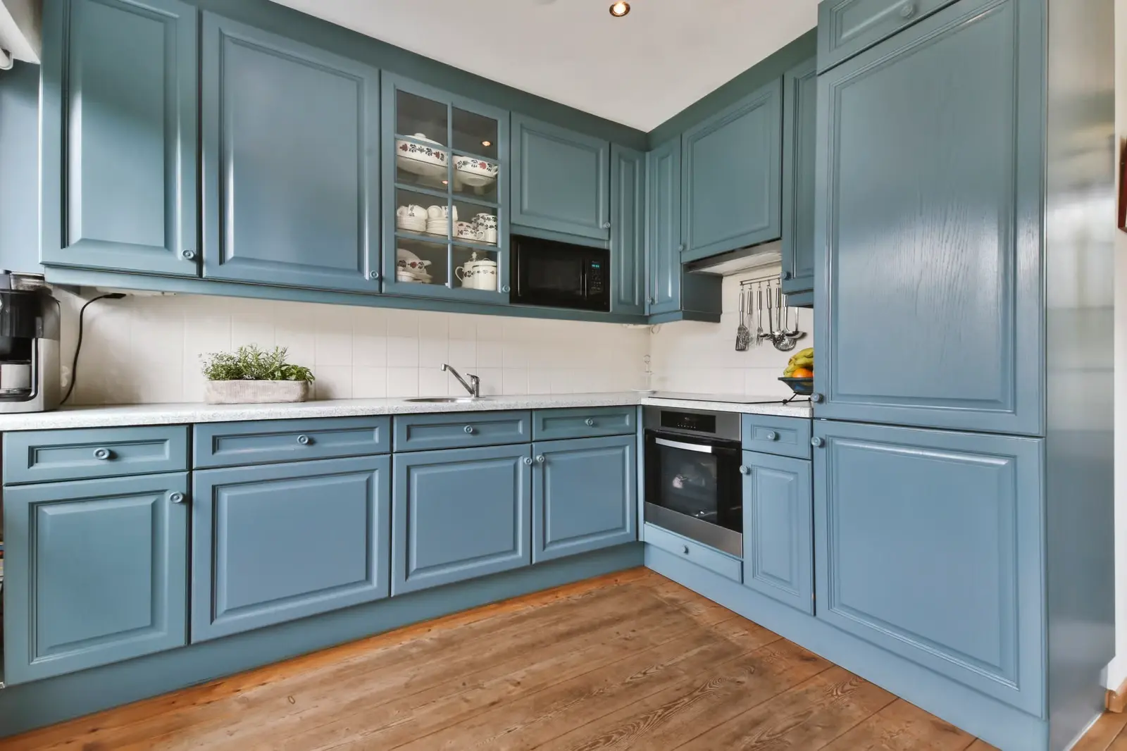 Kitchen with raised panel cabinets painted slate blue above warm wood floors