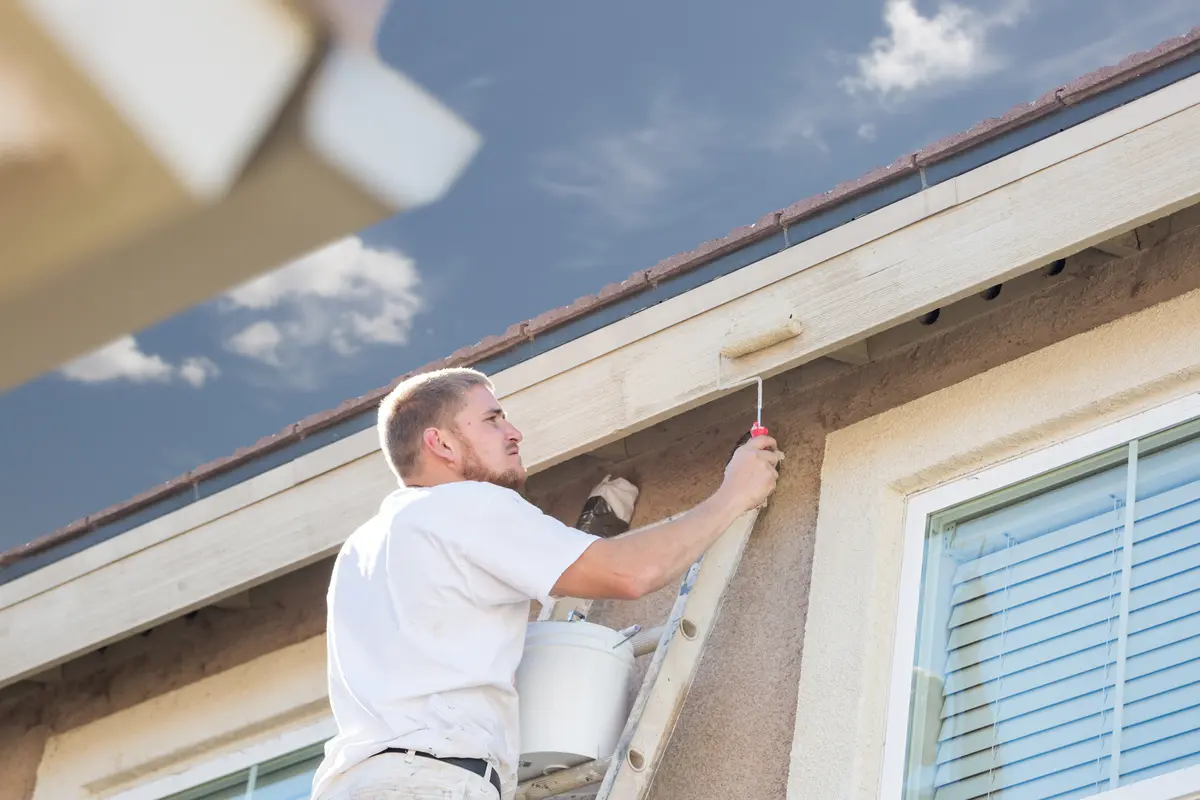 Painter on a ladder painting exterior trim