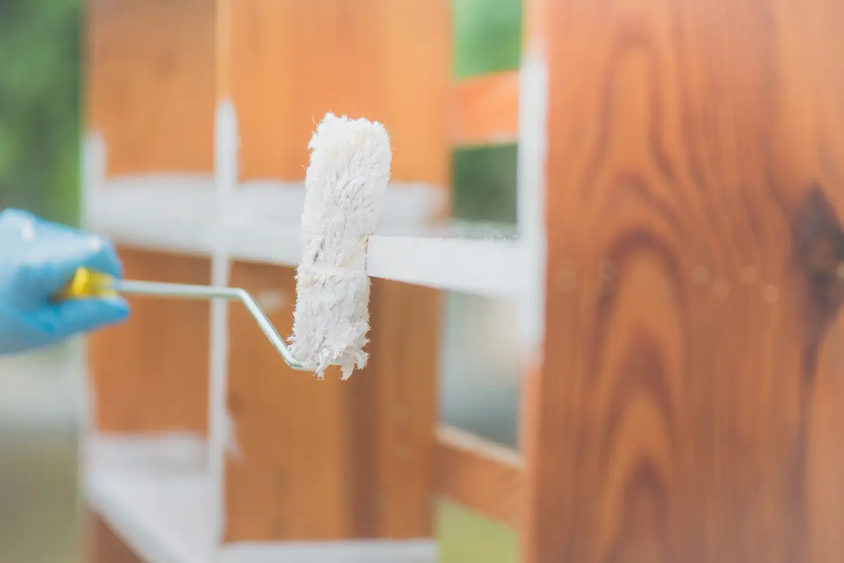 Small roller applying white paint to a wood cabinet