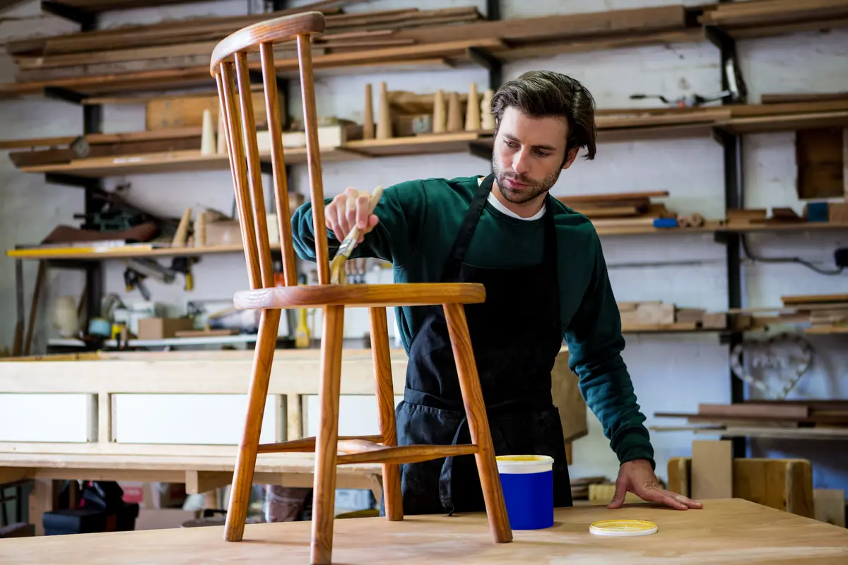 Painter refinishing a wood chair in a workshop