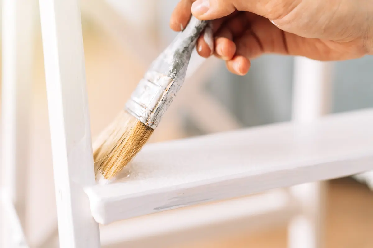Brush applying white paint to wood furniture