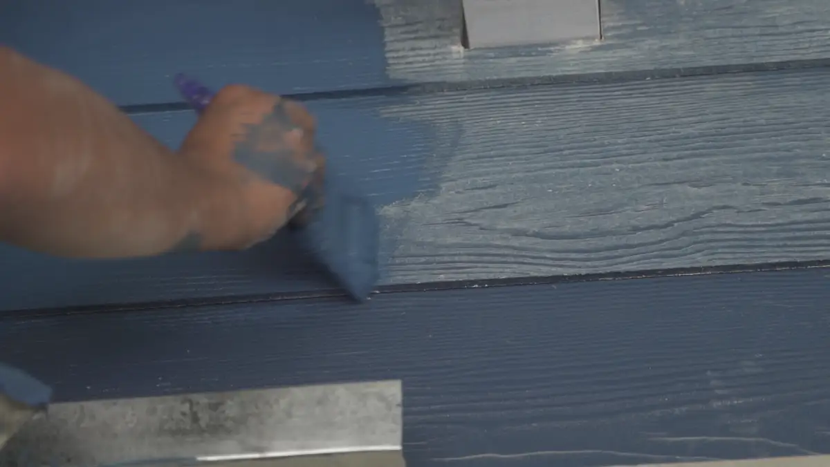Brush applying deep navy paint to a wood wall