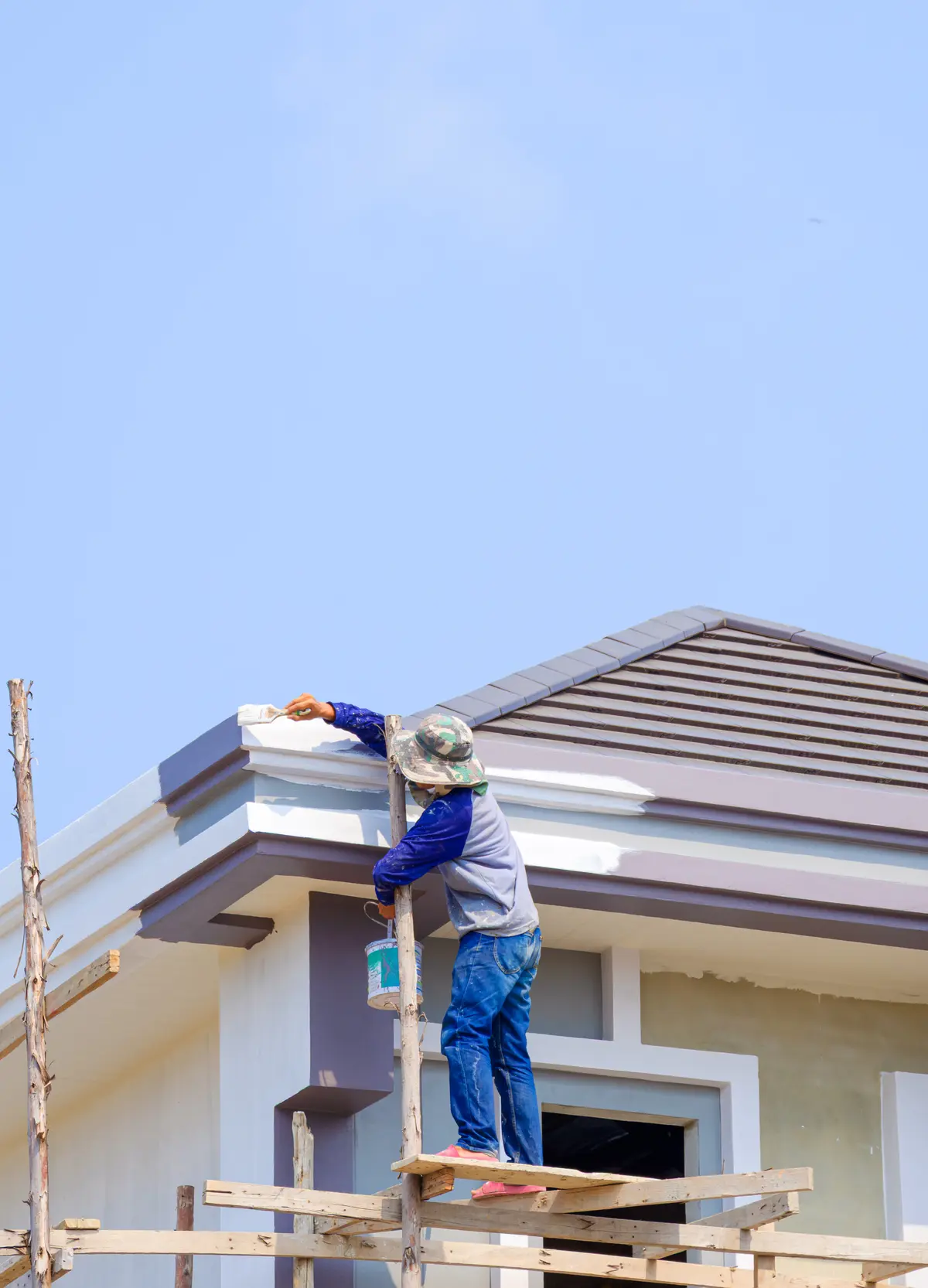 Painter on scaffolding painting roof eaves on a white home