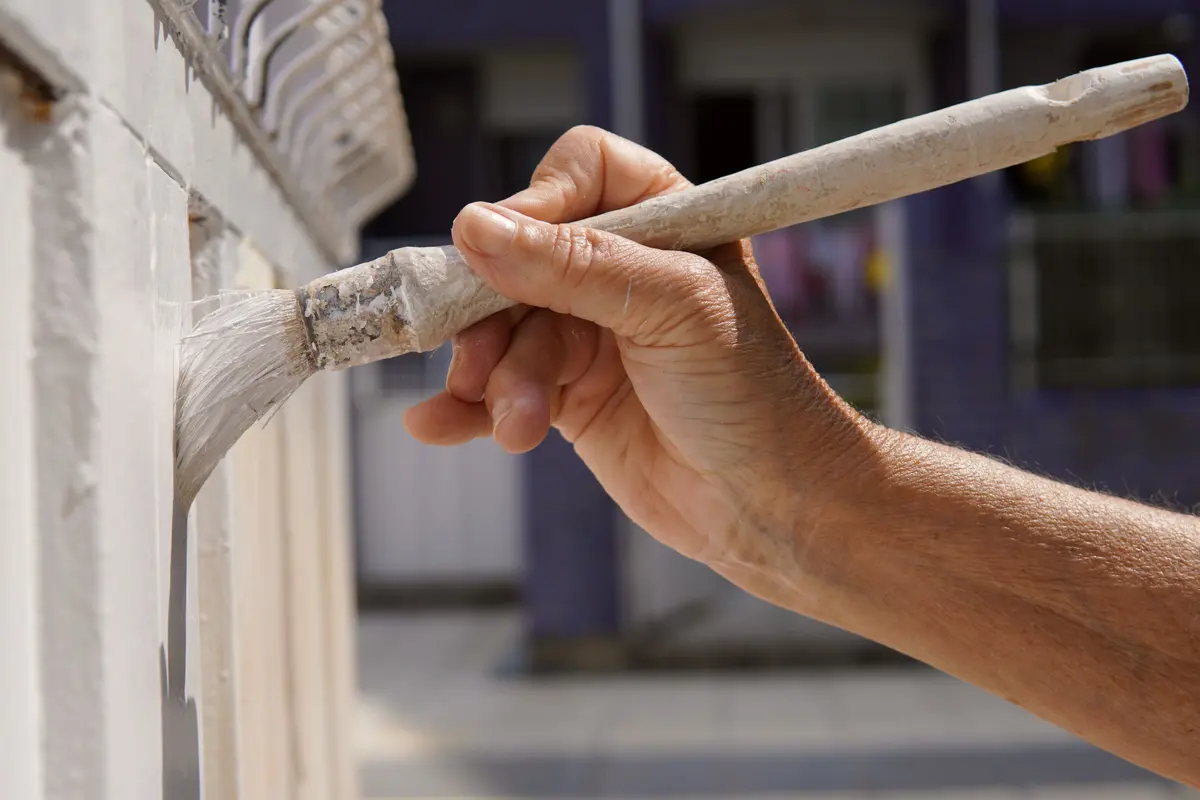 Close up of a brush applying white paint to trim