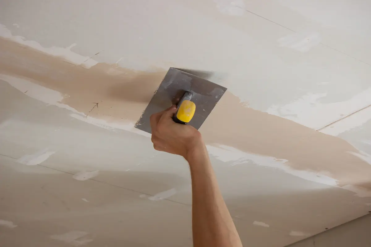 Trowel applying compound to a damaged ceiling