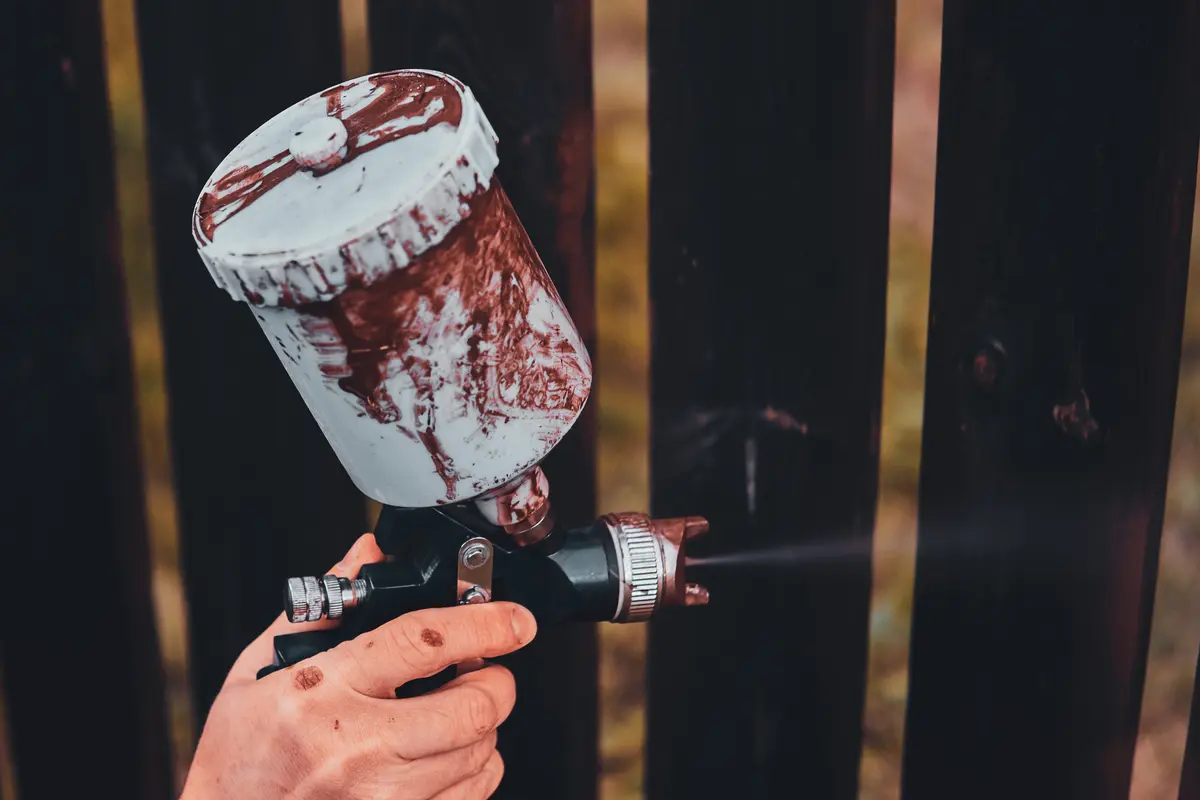 Close up of a spray gun coating fence boards