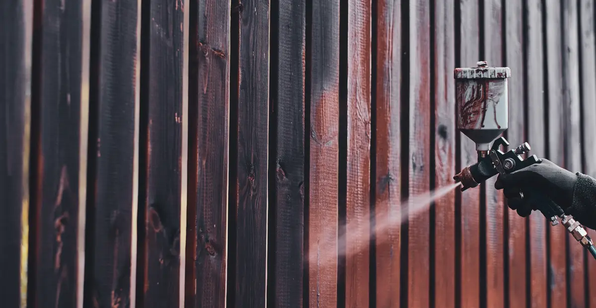 Painter spraying a dark finish on a wood fence